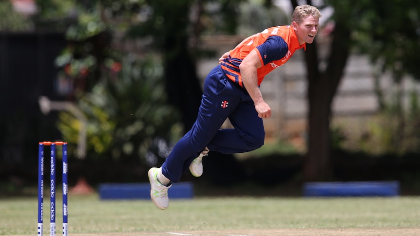 A fast bowler stares down the pitch in his follow-through after delivering a ball. 