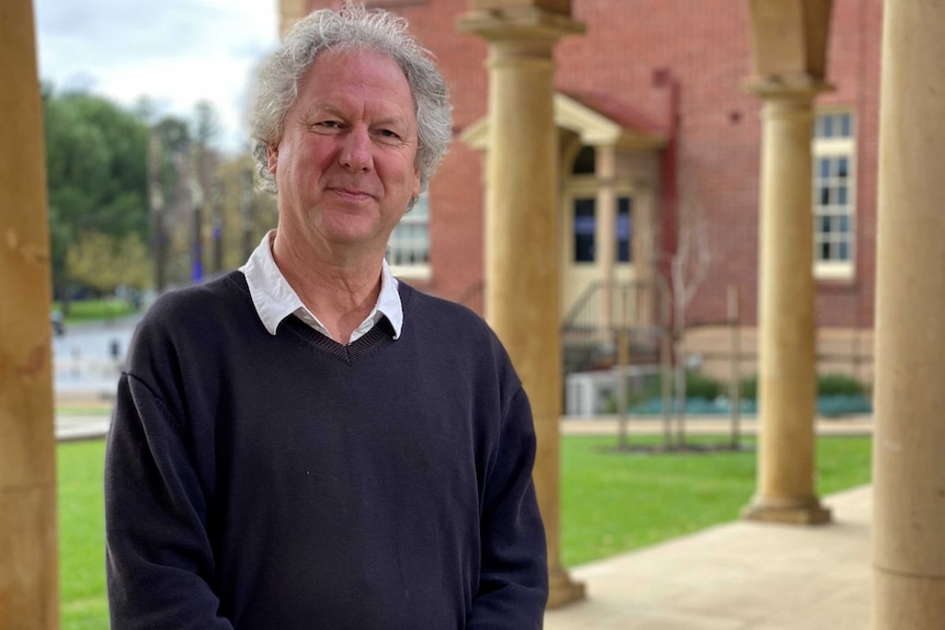 Clement Macintyre standing in a paved walkway next to a tan-coloured pillar