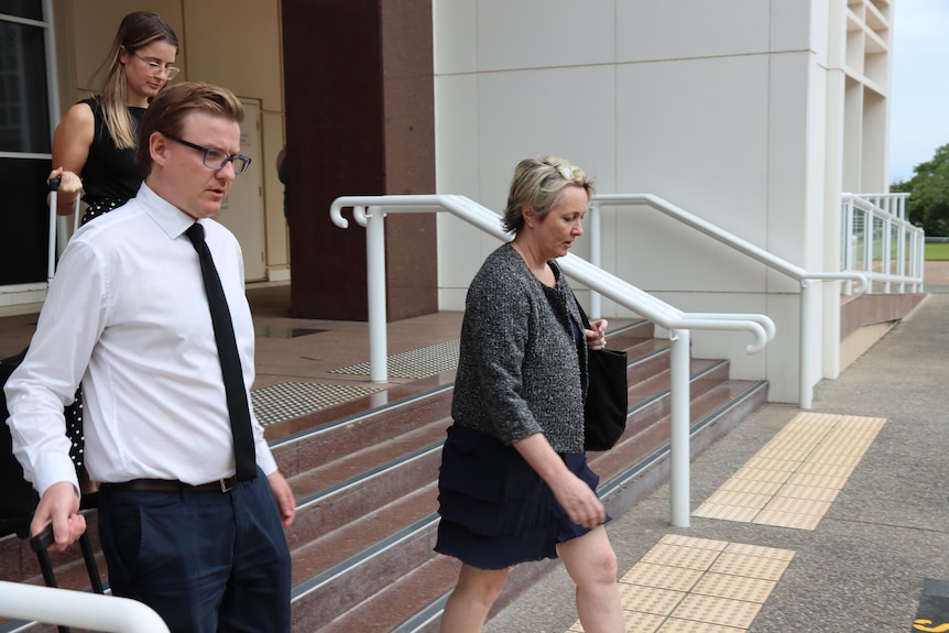 Two women and a man walk down the stairs of a courthouse. 