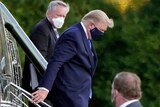 US President Donald Trump wearing a face mask, walking down the stairs of Marine One.