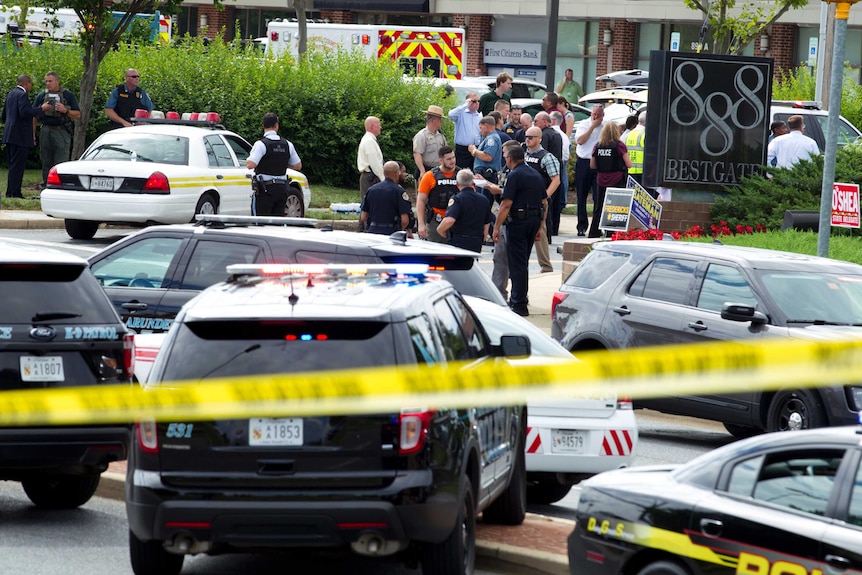 Police tape is seen in the foreground and police, authorities and emergency vehicles behind it.