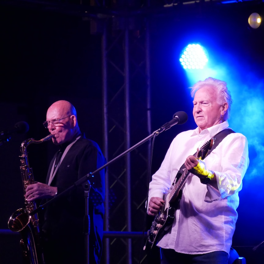 two men on stage playing the guitar and saxophone 