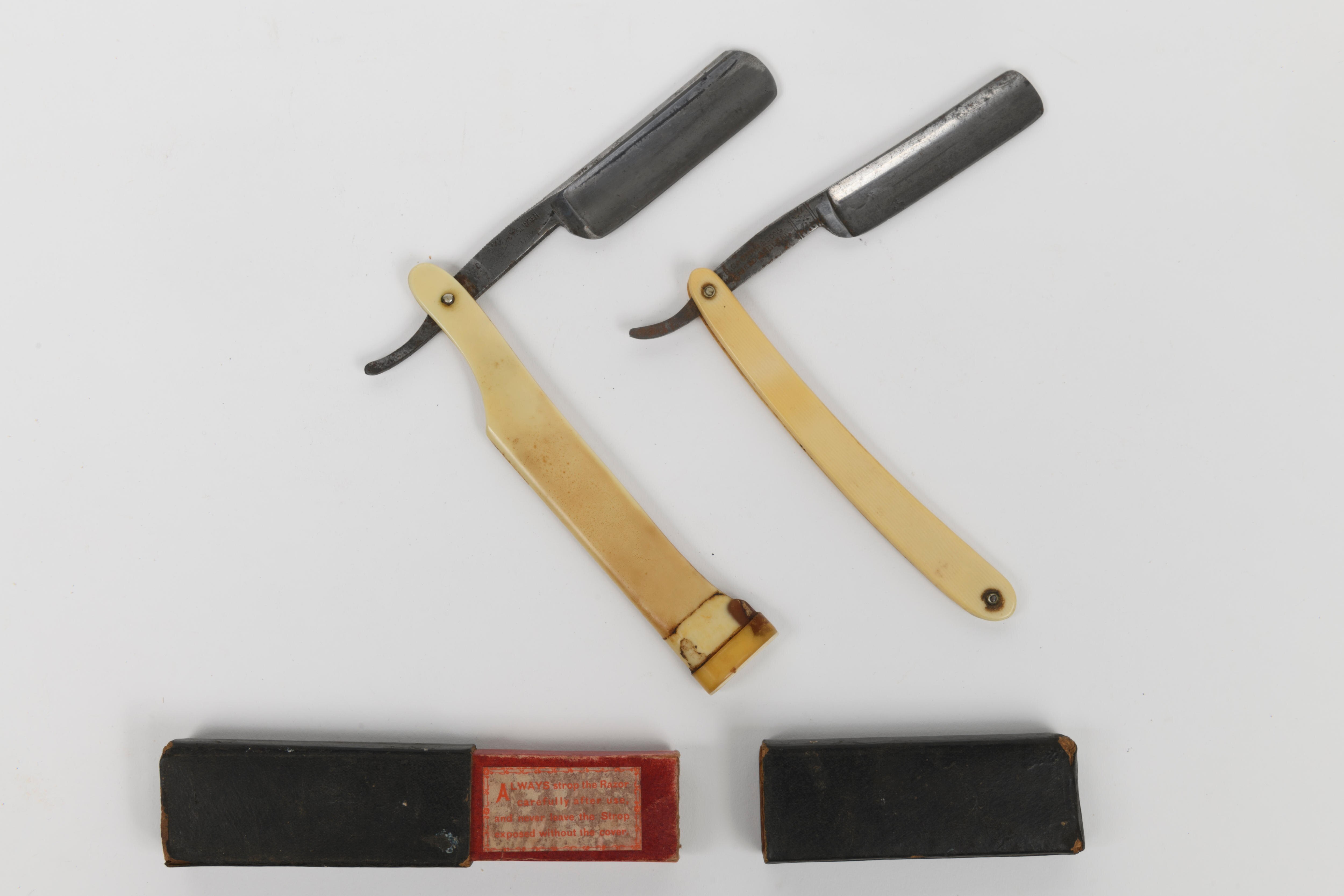 Two cut throat razors and small boxes on a white table.