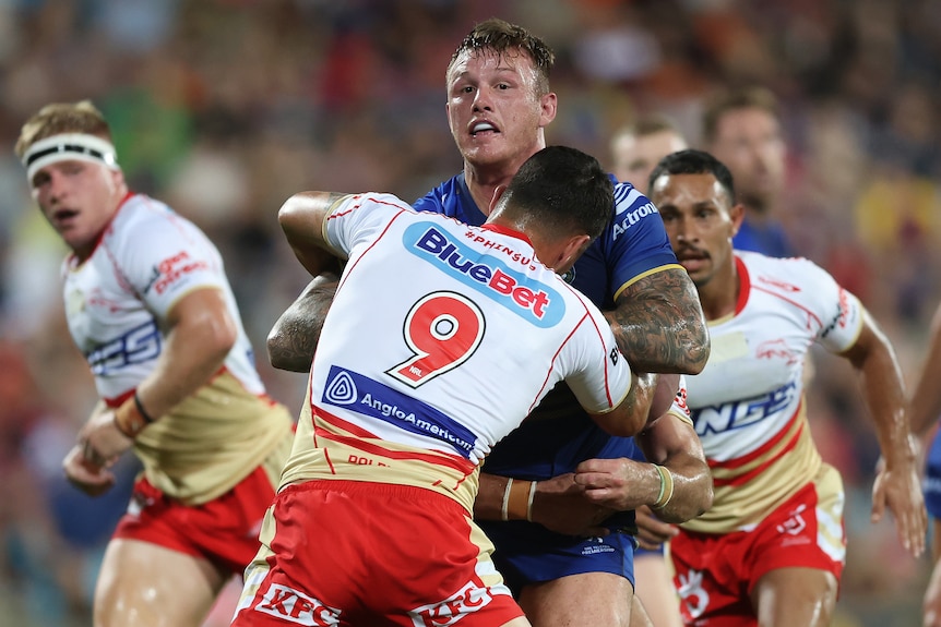 An NRL player runs the ball, and his tackled around the chest by an opponent