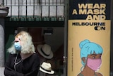 A blonde woman in a face mask next to a sign saying 'wear a mask and Melbourne on'.