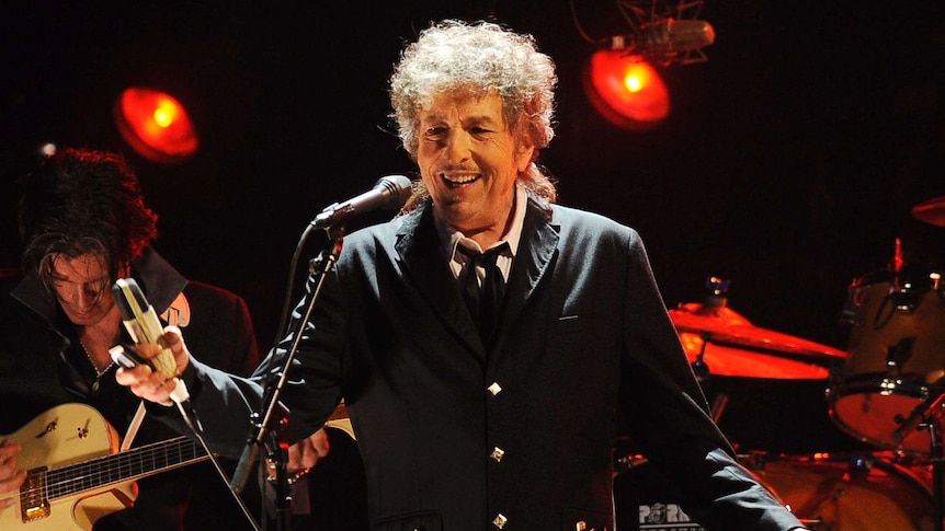 Bob Dylan stands on stage holding a microphone