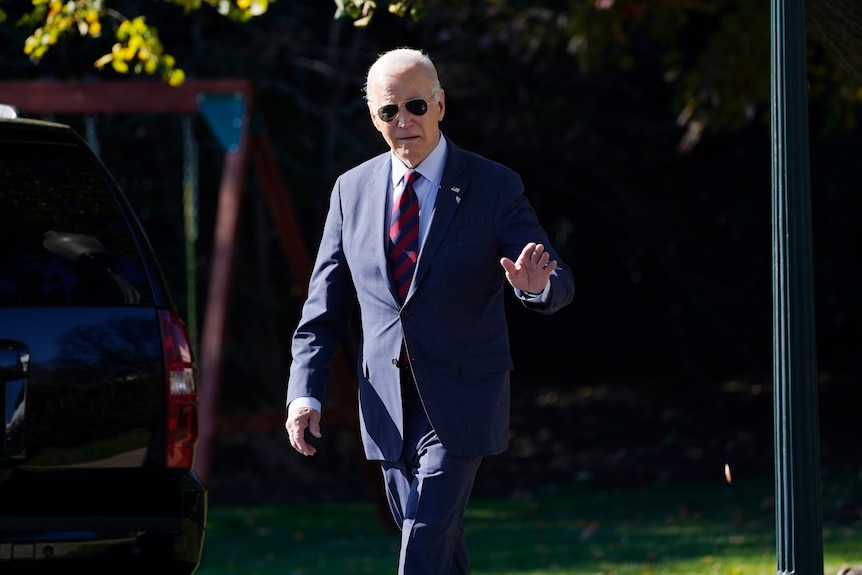 President Joe Biden walks across the South Lawn of the White House and waves.