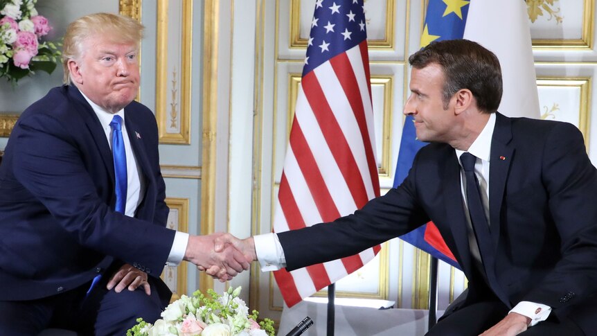 Seated with the US and France flags behind them, Donald Trump frowns as he shakes Emmanuel Macron's hand.