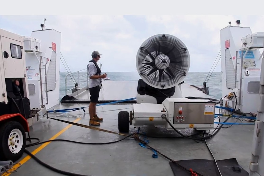A man on a boat standing next to a big fan taking notes