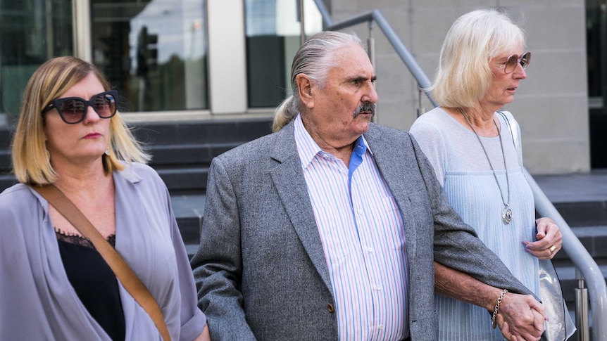Hervey Alan Harms walks down stairs outside a Perth court, flanked by two women.