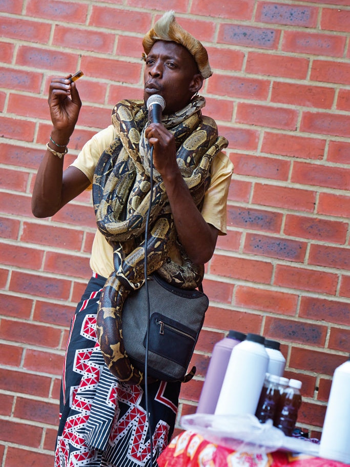 An African man has a snake wrapped around his neck and holds onto oil.