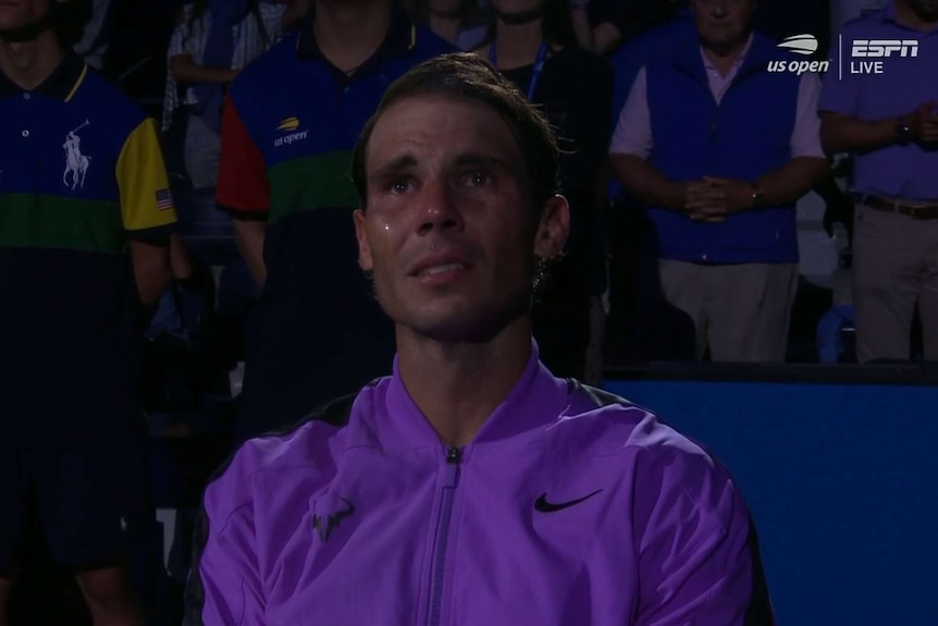 Rafael Nadal is in a dark area with people standing behind him as tears run down his face
