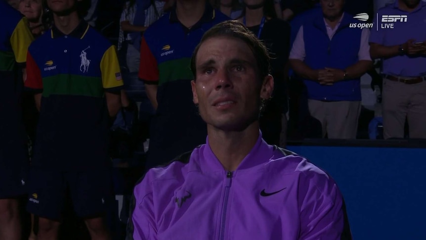 Rafael Nadal is in a dark area with people standing behind him as tears run down his face