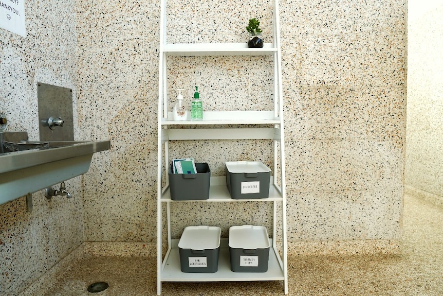 A shelving stand in school bathroom with soap and tubs of hygiene products.