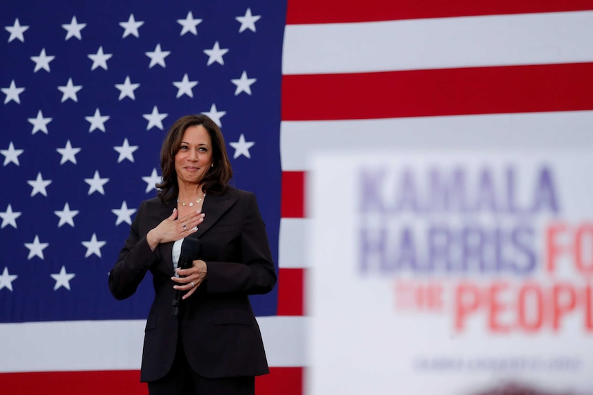 US Senator Kamala Harris holds her hand to her chest in front of an American flag
