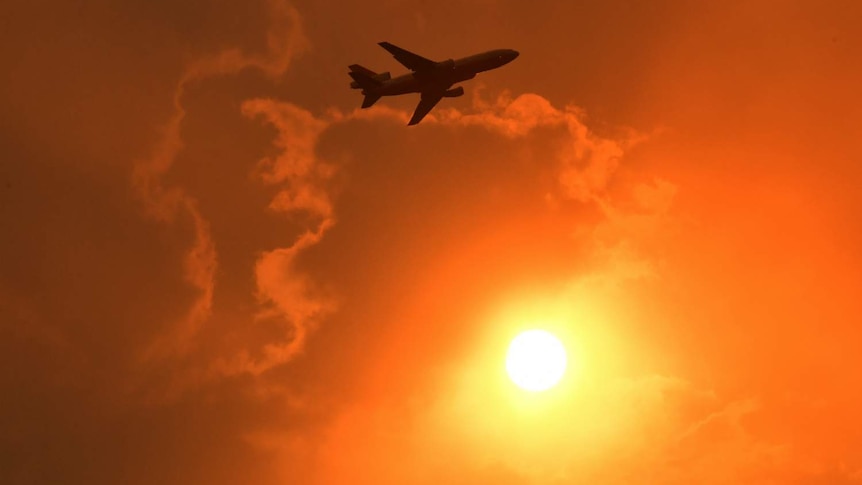 The silhouette of a plane can be seen, with a red sky behind it