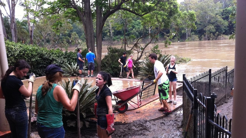 Volunteers help clean up muddy backyard and pool at flooded house on Brisbane River at Chelmer.