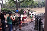 People clean up muddy backyard and pool at flooded house on Brisbane River at Chelmer