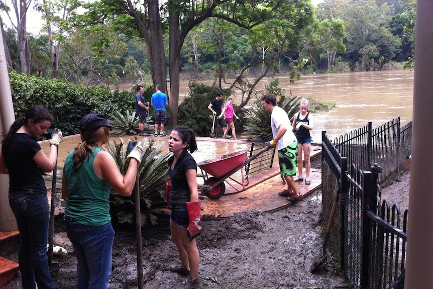 Volunteers help clean up muddy backyard and pool at flooded house on Brisbane River at Chelmer.