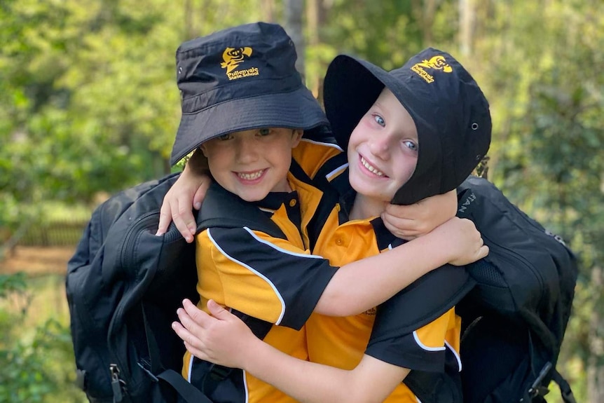 Twins Nixon and Mitchell Conradi hug each other with their backpacks and hats on.
