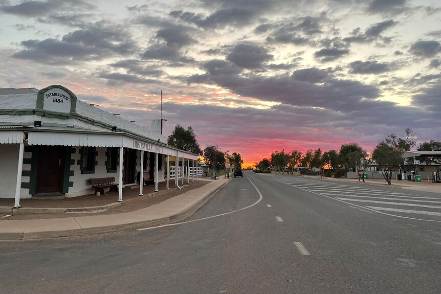 Birdsville Hotel sits along an empty road, with a colourful sunset in the background