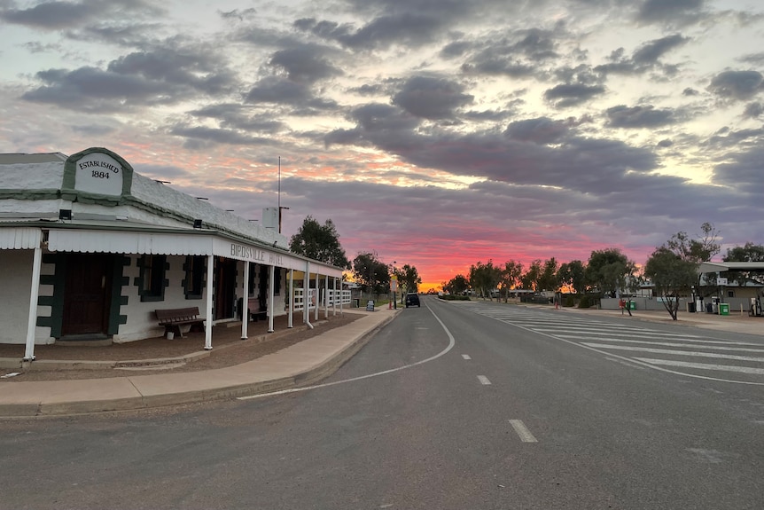 Birdsville Hotel sits along an empty road, with a colourful sunset in the background