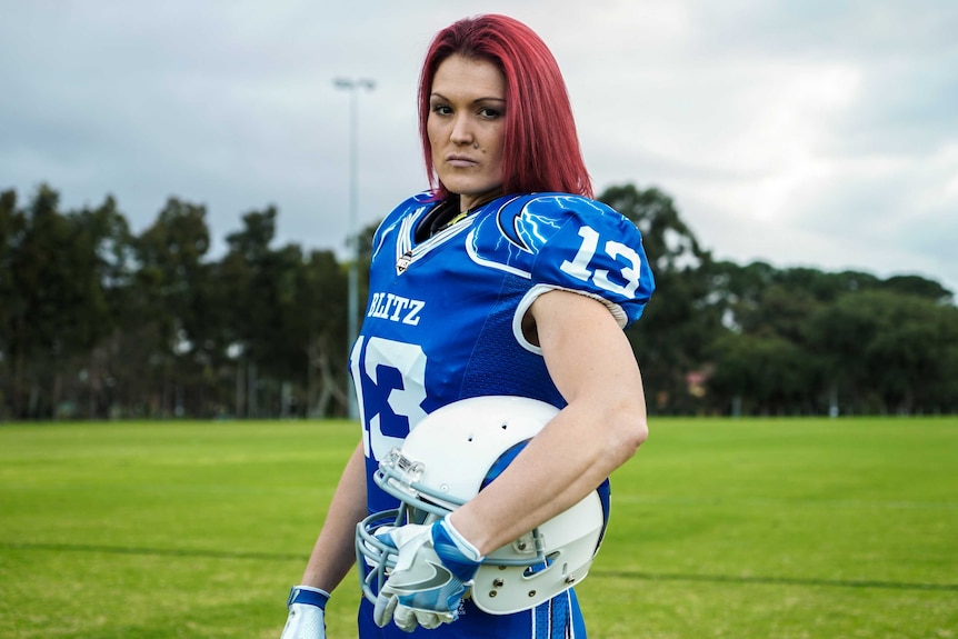 Rhyanna Edbrooke poses for a photo in her blue uniform, standing side on and holding her helmet.