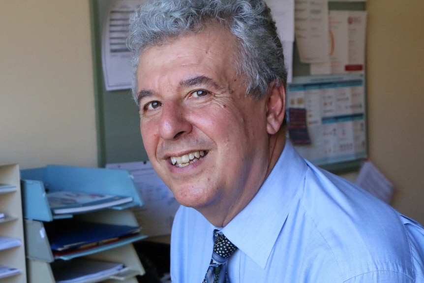 A man wearing a blue shirt and tie smiles for a photo.