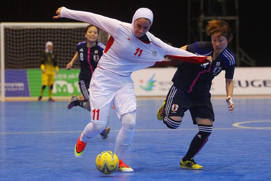 Women players tug at shirts while wrestling for a futsal ball