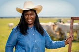 A woman in a cowboy hat stands in a paddock with cows behind her