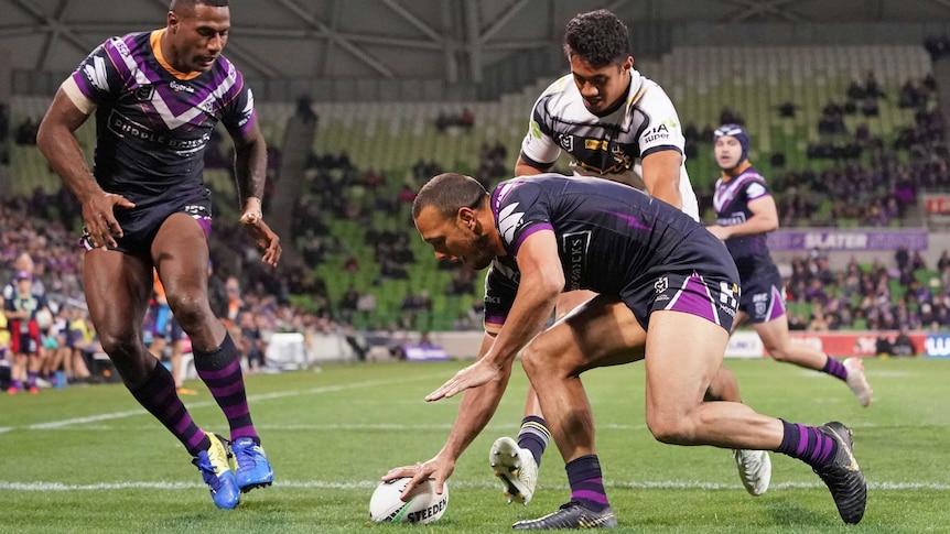 An NRL player plants the ball down over the try line as a teammate and opponent watch on.