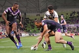 An NRL player plants the ball down over the try line as a teammate and opponent watch on.