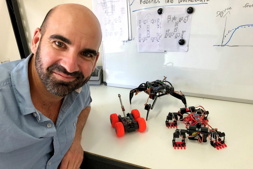 Man sitting at a desk with three different types of robots beside him.