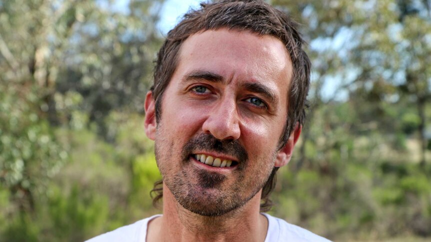 Gareth Liddiard smiles, standing outside with trees behind him.