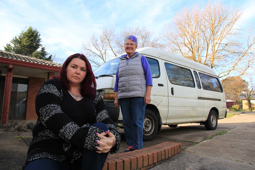 A woman sitting on the ground in front of an old van with another woman  standing behind her