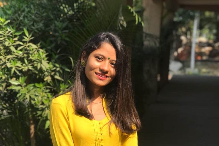 Woman in yellow salwar kameez and green bindi on her forehead smiles at camera.