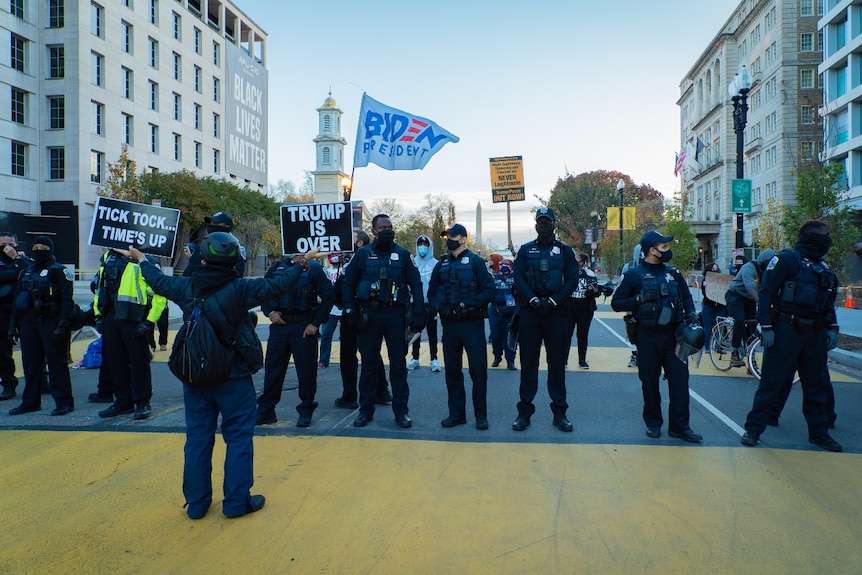 A person holding up black signs in front of a line of police officers