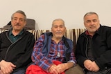 Three men sit together on a couch.