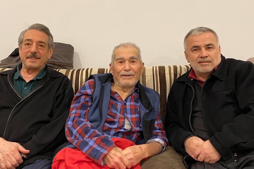 Three men sit together on a couch.