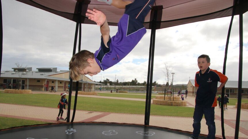 A student wearing a purple shirt does a somersault on a trampoline as another child watches on.