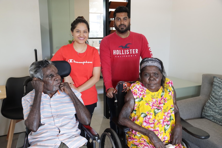 Two people in wheelchairs are in a room with their care givers. The room is newly built.