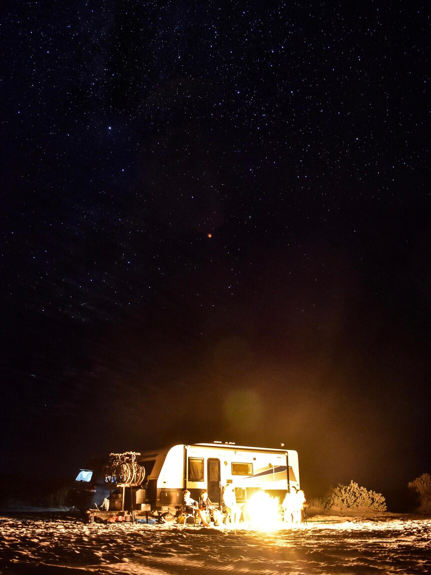 A campervan under the stars beside a campfire. 