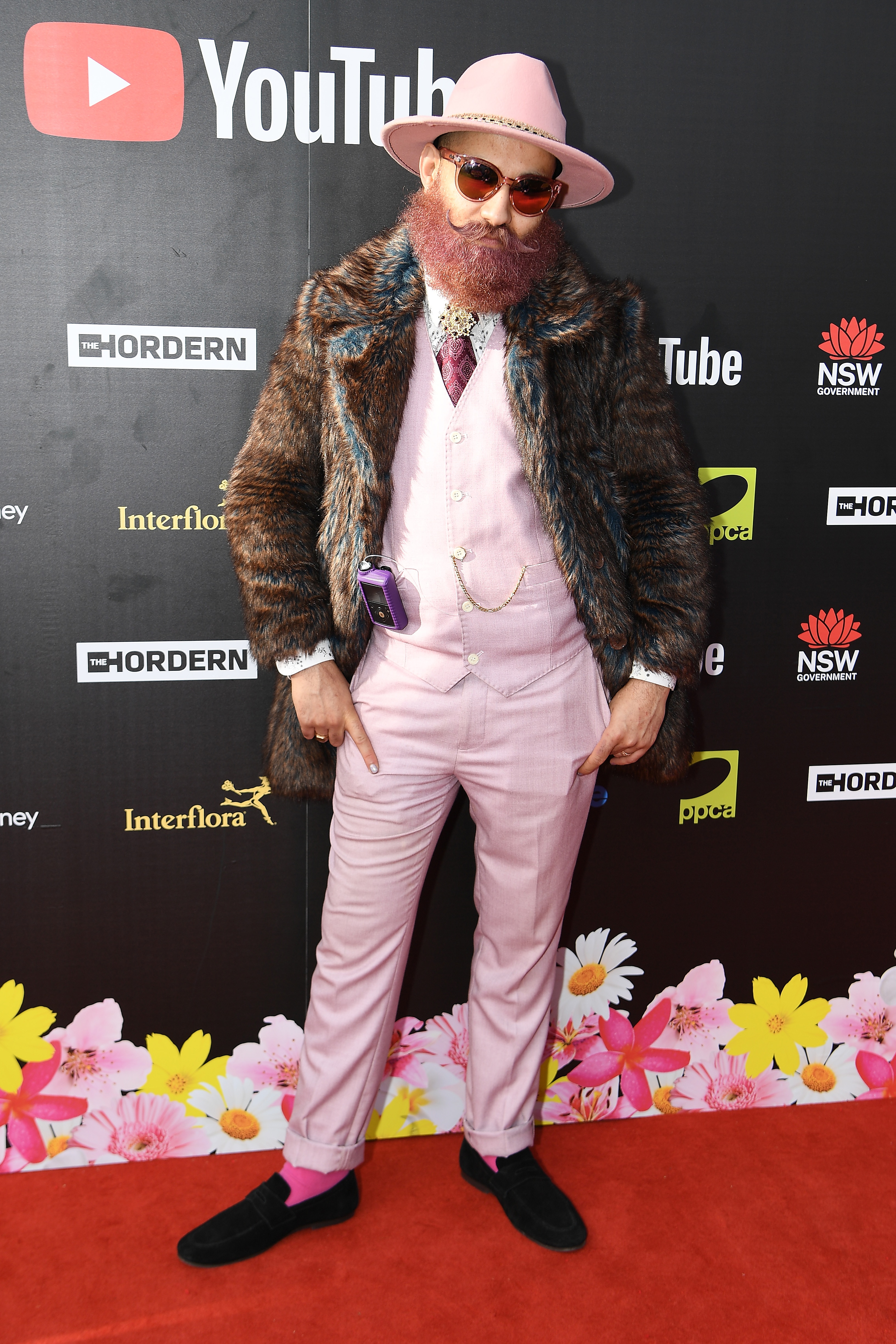 James Tawadros portant un costume rose pâle avec un manteau de fourrure