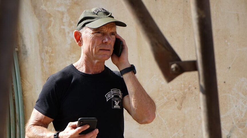 A man speaks on the phone wearing a t-shirt that says Free Burma Rangers.