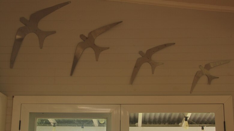 A series of metal birds mounted on the interior wall of a home like flying wall ducks.