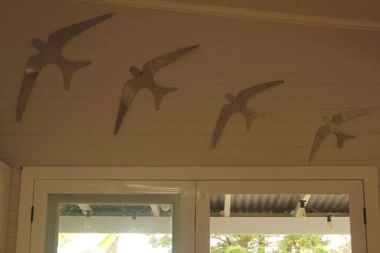 A series of metal birds mounted on the interior wall of a home like flying wall ducks.