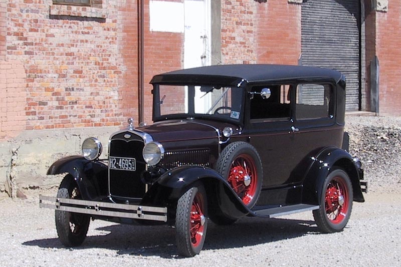 A 1930s car with soft roof and spare wheel attached to driver's side.