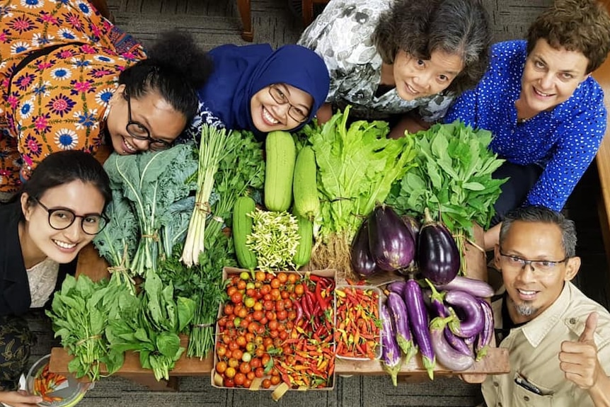 Six people gathered around a table of vegetables.