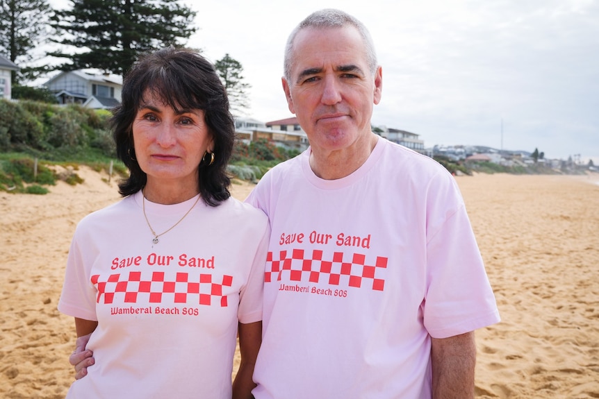 A woman and a man in pink shirts on a beach looking at the camera.