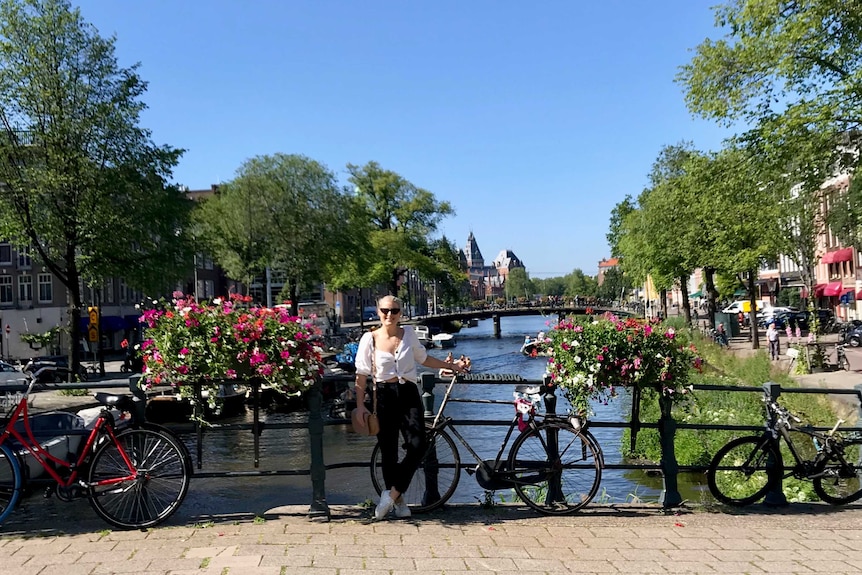Brittany Mason stands next to bicycles on a river in the centre of Amsterdam.